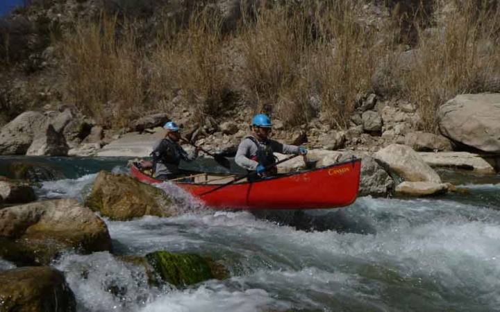 two gap year students paddle a canoe through whitewater on an outward bound expedition in texas